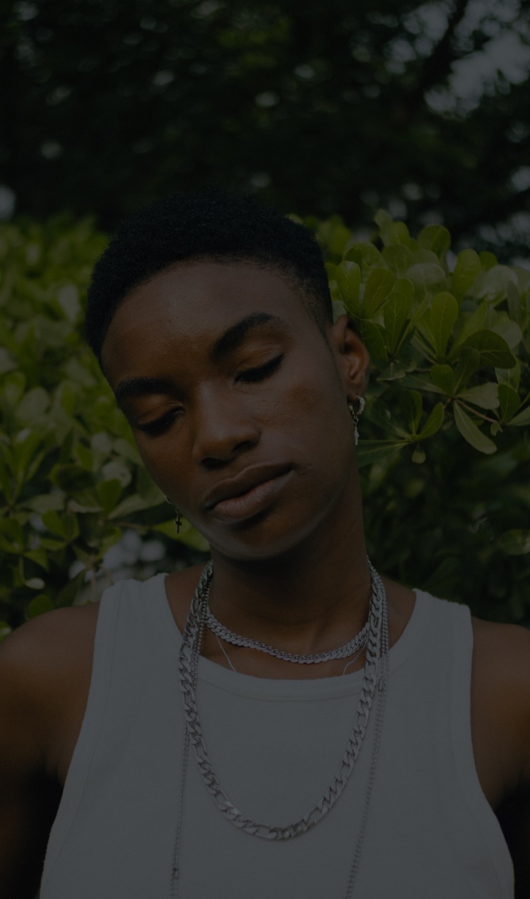 A person stands in front of greenery with a darkened overlay with their eyes closed.