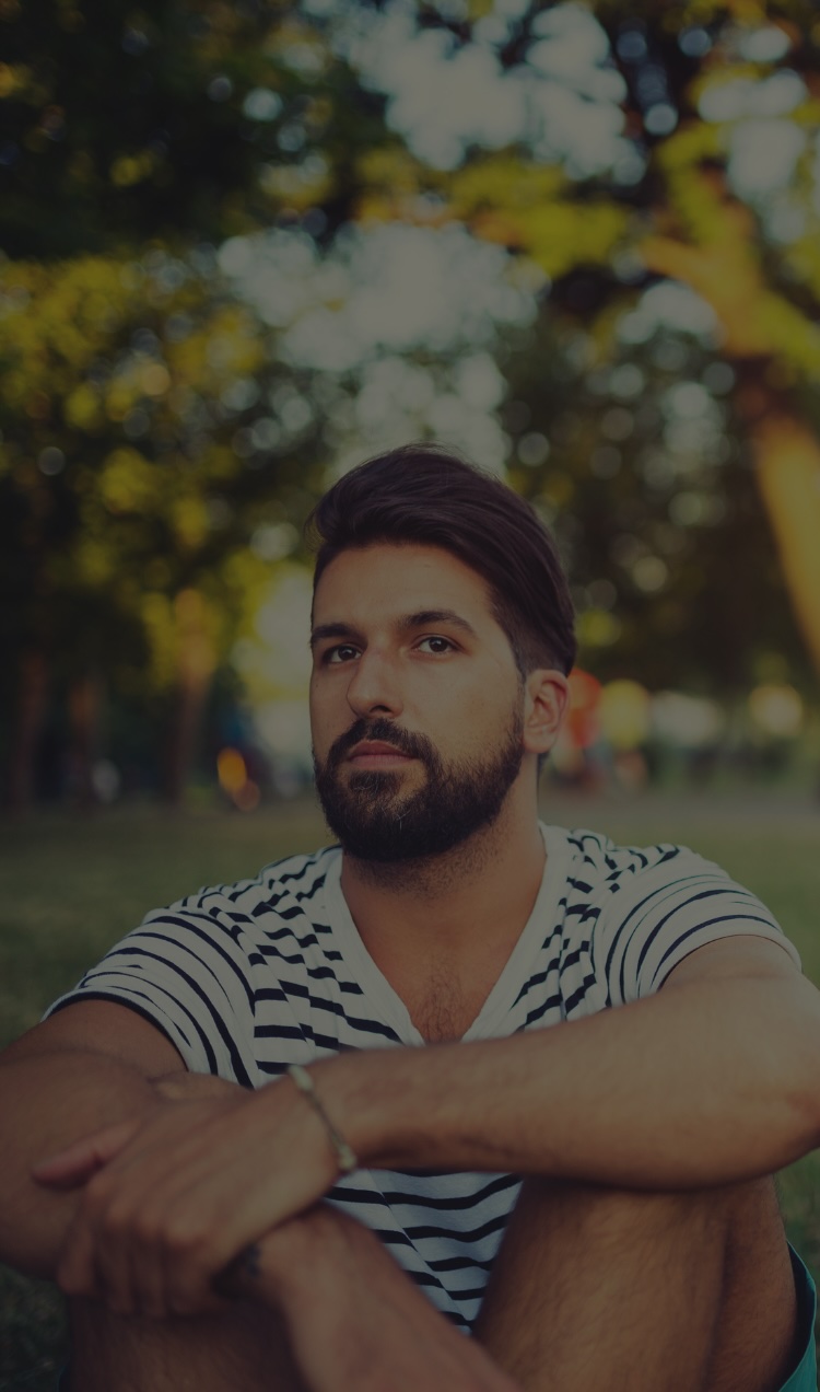 An anxious man sits outside on a summer day in a park.