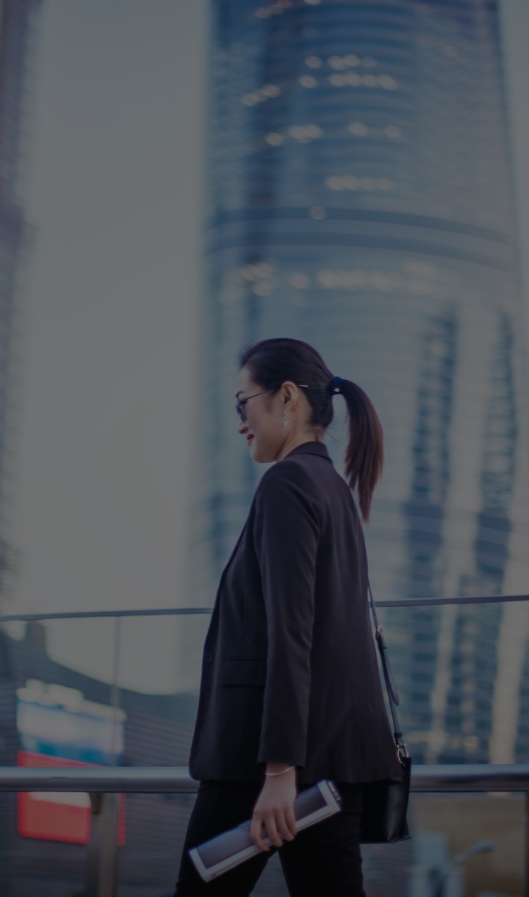 A woman walks to work with a bag and a newspaper while crossing a bridge in the city.