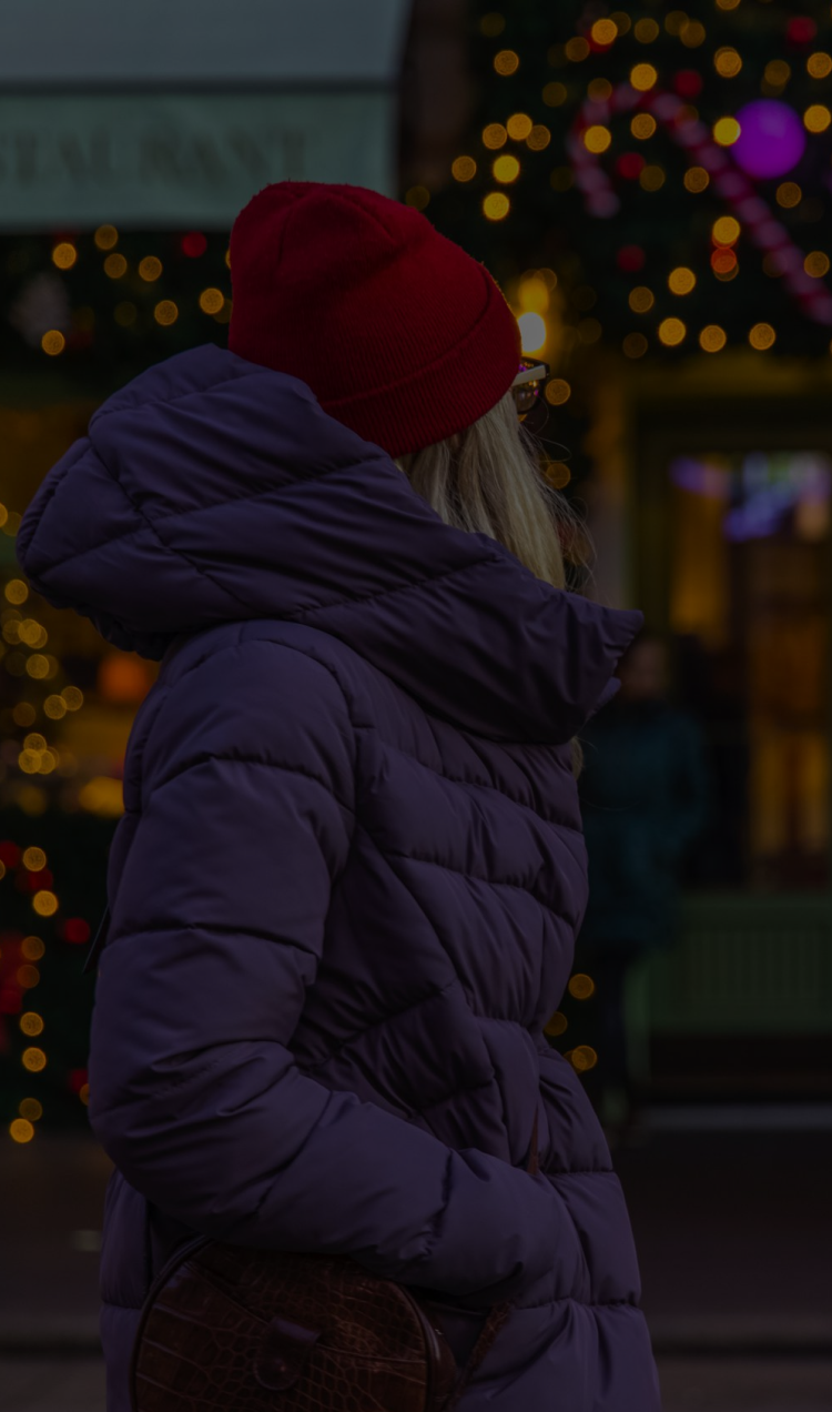 A woman passes by a shopping center decorated with holiday lights.
