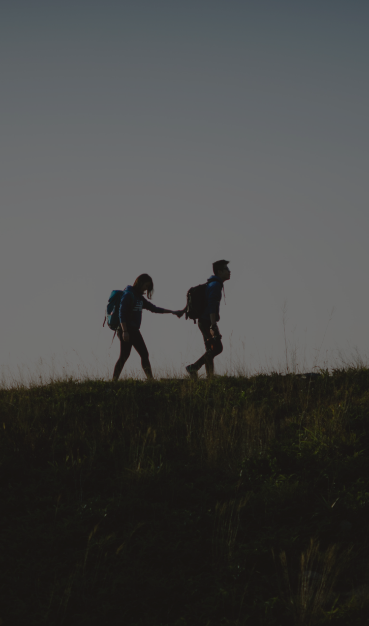 A couple walking across a hilltop with hands stretched toward each other.